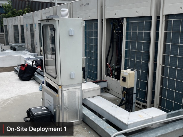 The MV2 measurement cabinet on a rooftop beside a row of VRF outdoor units, one opened for sensor connection.