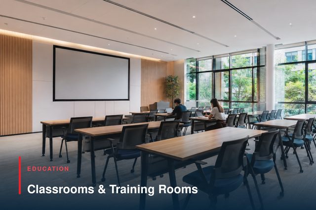 A daylit teaching room with rows of tables facing a projection screen.