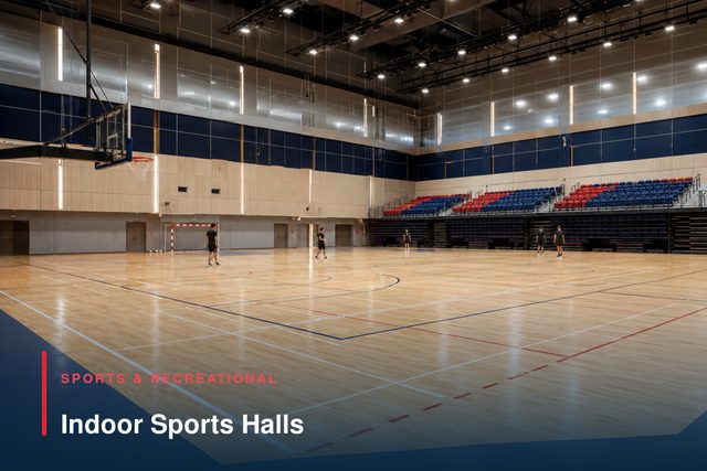A double-height indoor sports hall with a sprung timber court and retractable spectator seating.