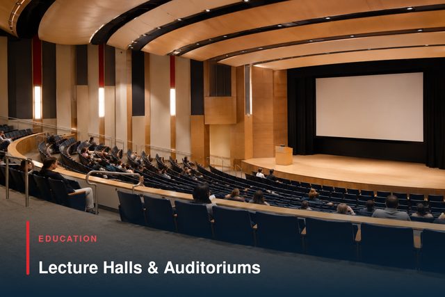 A tiered lecture theatre with banked seating and a stage with a projection screen.