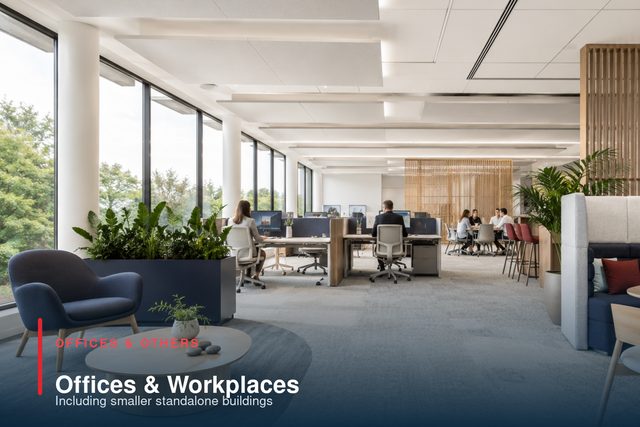 An open-plan office with workstations along a glazed elevation, planting and a booth seat.